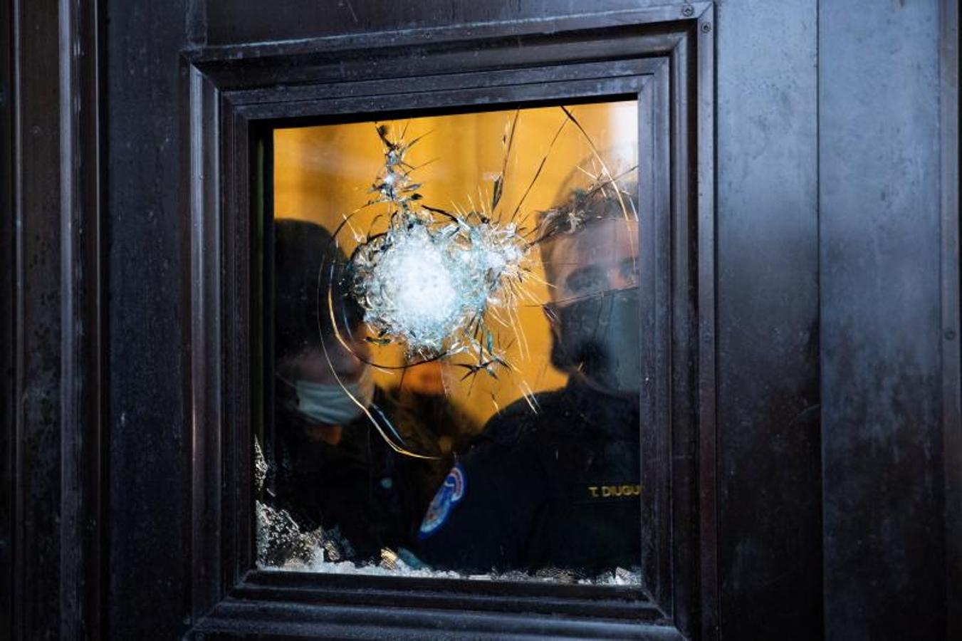 Dos policías observan a través del vidrio roto de una de las puertas del Capitolio
