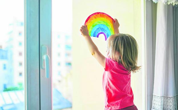 Una niña coloca el dibujo de un arco iris contra el cristal de una ventana. /e. pokrovsky