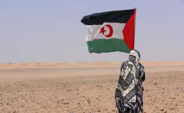 Una persona sostiene una bandera de la República Árabe Saharaui Democrática ante el muro que separa el Sáhara Occidental de Marruecos. /natalia de La rubia
