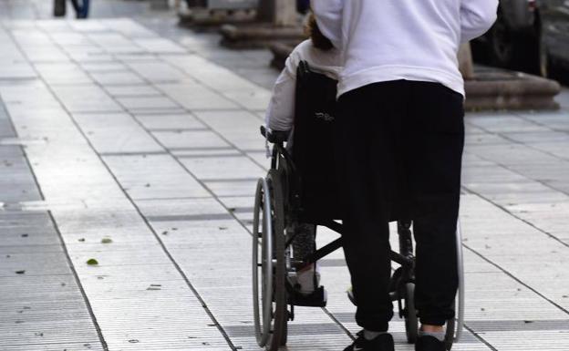 Imagen de archivo de una persona empujando a un dependiente en silla de ruedas. 