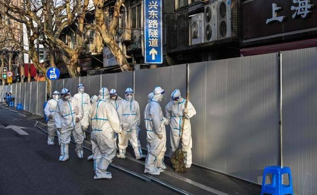 Un grupo de trabajadores vestidos con trajes de protección pasan junto a una barrera colocada para confinar un área residencial de Shanghái tras la detección de un brote de covid, en marzo de este año.